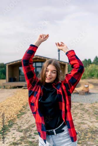 Portrait of a young happy girl dancing on the background of large wooden cottage in the forest steppe