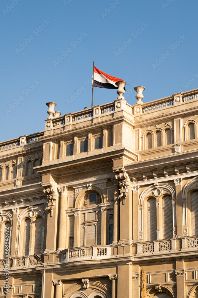 Egyptian flag waving on top of a government building with the blue sky behind