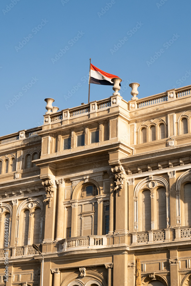 Obraz premium Egyptian flag waving on top of a government building with the blue sky behind