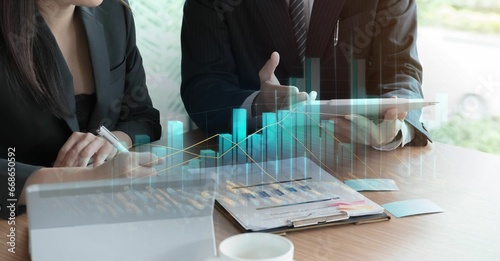 Mujer y hombre de negocios, trabajando en su despacho, con sus tablets, mujer tomando nota con su taza de café, gráfico de barras representando las ventas o evolución de inversiones. 