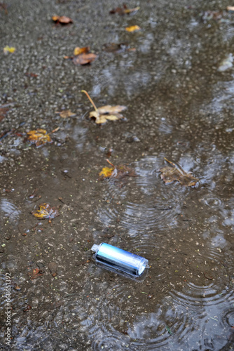 A metallic electronic cigarette vape has been left, discarded in a puddle in the rain.