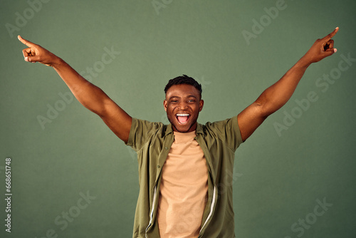 Cheering in success. Joyful handsome african guy wearing casual yellow t-shirt and unbuttoned shirt posing over green background with hands wide open. Sincere human reaction on amazing news