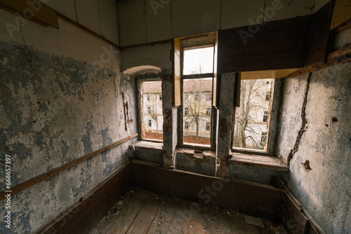 From above view of interior of room with wooden floor structure shabby unkept worn out walls peeling paint and windows overlooking outside abandoned building with trees in daylight photo