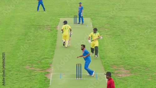 Two Yellow Team Batsmen Successfully Scoring Cricket Runs, While the Bowler Player Waiting for the Ball to Return From a Field Player. Professional Cricket Match TV Broadcast Footage photo