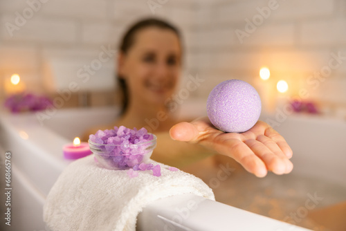 woman relaxing in bathtub in candle light and using bath bomb with sea salt crystals for body skin moisturizing. home spa, skincare photo