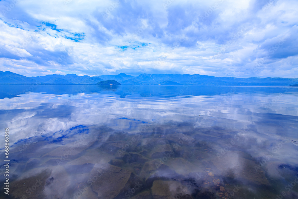北海道、屈斜路湖の雲に覆われた空を鏡の湖面に反射する風景。