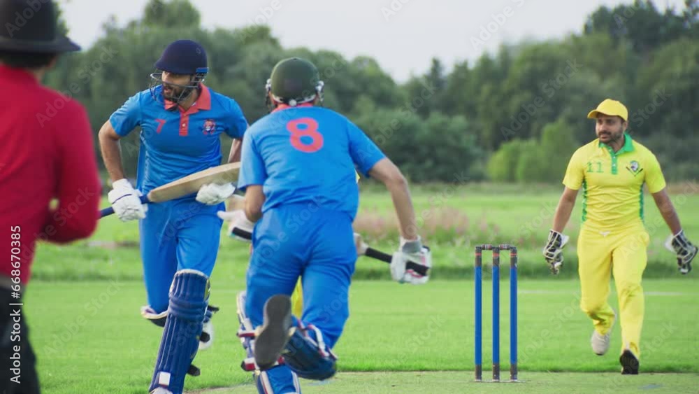 Professional Indian Cricket Player in Blue Uniform and Protective Gear Hitting the Ball and Defending the Wicket. Athletes Practicing on a Green Pitch on a Warm Afternoon