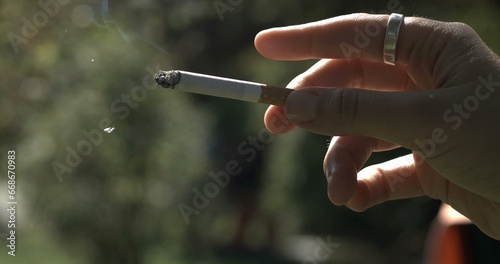Finger tapping into cigarette ash falling off captured in. Close-up hand holding addictive substance photo