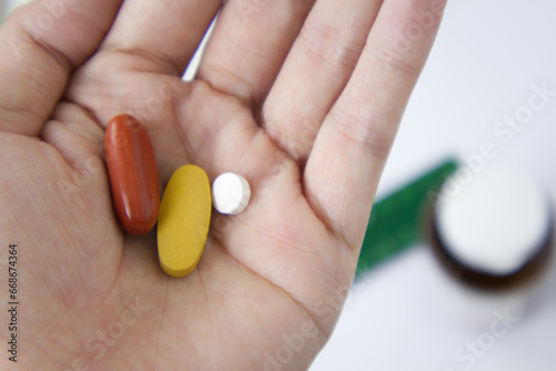 Various type of vitamins on women hand before taking as daily routine. Blurring bottle and pack of vitamin on white background in the back.