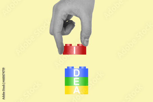 Idea letters on colorful buildings blocks stacking by a hand of artist on pastel yellow background.