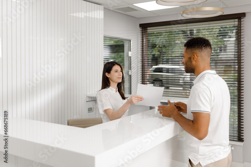 Modern medical clinic guy came for a visit to doctor at reception desk he signed on paper then go to the doctors cabinet