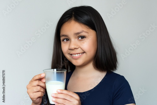 girl with a glass of milk. little girl stands in the room with a transparent glass of milk, the girl drinks milk and smiles