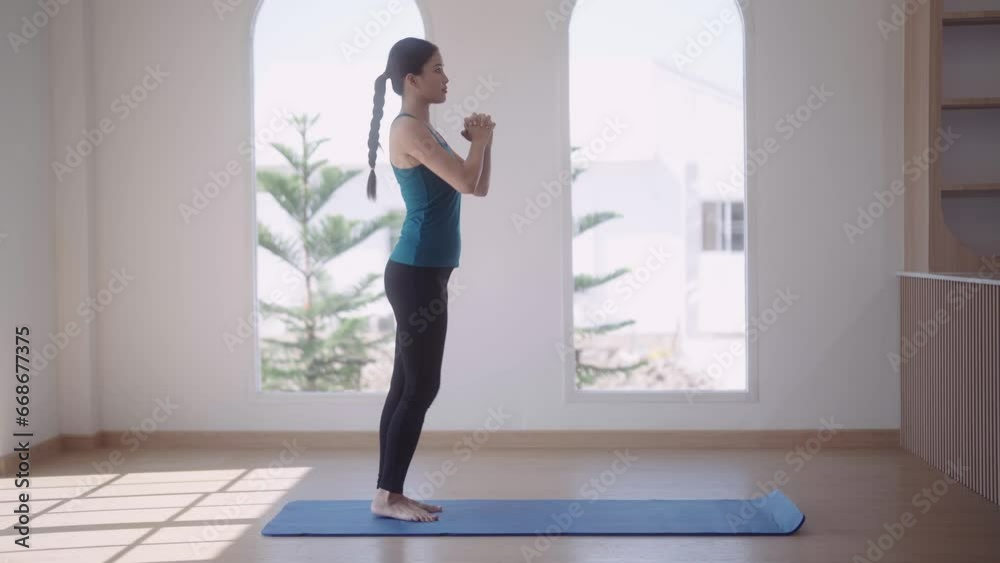 An Asian young woman in workout attire is exercising by stretching her legs forward on a mat for a healthy workout routine at her home, strengthening her overall health