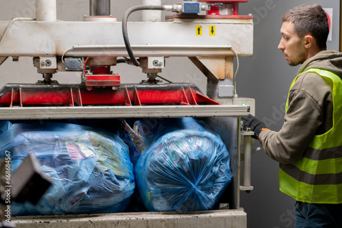 Fotografie A recycling plant employee in uniform puts bags of garbage into special press ma