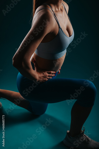 Powerful fit girl in a dark studio shows her incredible body transformation, muscular torso, and six-pack abs as she exercises and trains.