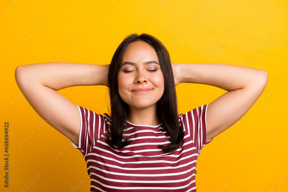 Photo of satisfied sleepy person with straight hairstyle wear striped t-shirt holding arms behind head isolated on yellow background