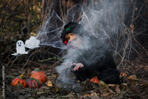 Happy Halloween. little sorcerer brews potion in witch's cauldron, casting spell. Boy having fun, Halloween party outdoor, autumn