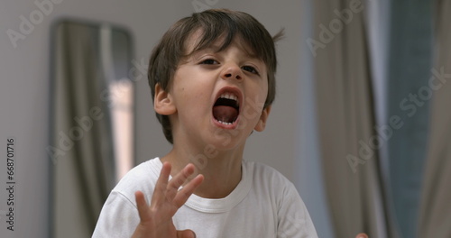 Angry child yelling and screaming at camera in super slow-motion. Upset male caucasian kid in tantrum mode photo