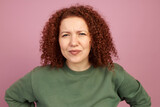 Studio portrait of puzzled suspicious female standing over pink background with hands on waist, squinting eyes trying to figure out complicated situation, uncertain with making right decision