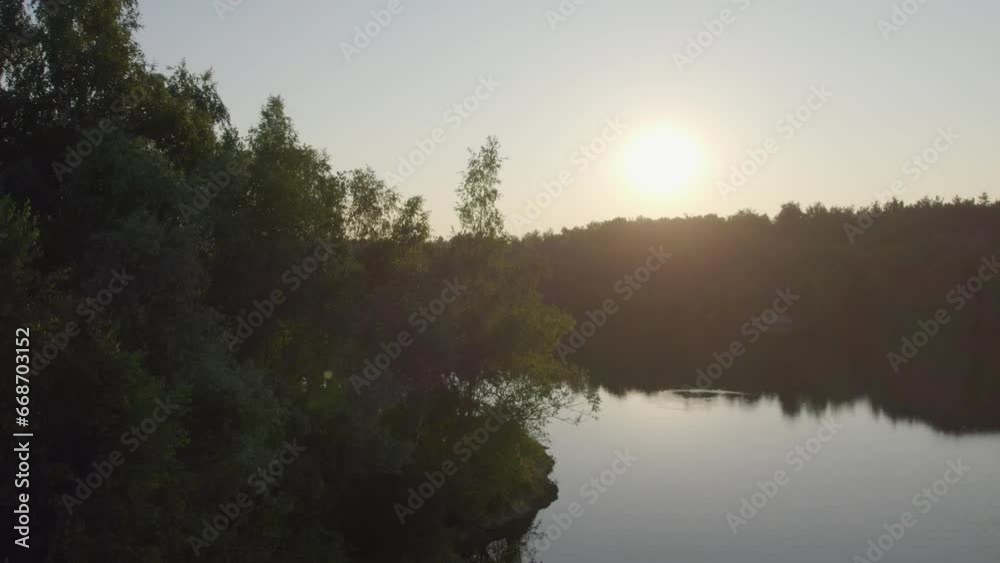 In a gentle ascent, the aerial view transitions from the concealment behind a solitary tree to reveal a breathtaking sunset over a serene forest lake. The evening sky, painted with strokes of crimson In a gentle ascent, the aerial view transitions from the concealment behind a solitary tree to reveal a breathtaking sunset over a serene forest lake. The evening sky, painted with strokes of crimson