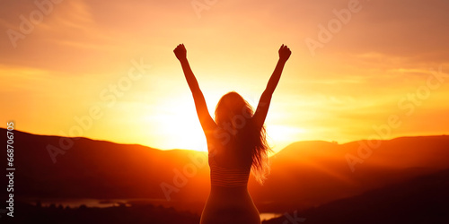 Silhouette of woman with arms raised up in beautiful sunset landscape