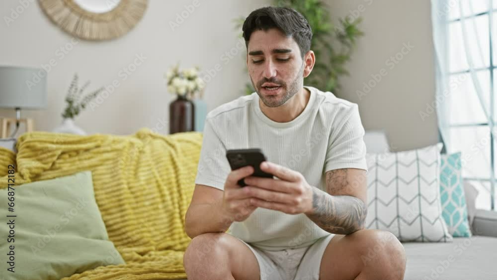 Young hispanic man arguing by smartphone sitting on sofa angry at home Young hispanic man arguing by smartphone sitting on sofa angry at home