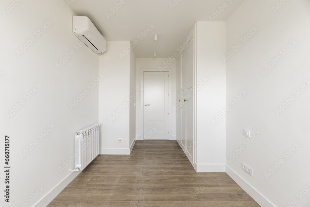 Empty room with air conditioning unit, built-in wardrobes with white wooden doors matching the access door and baseboards