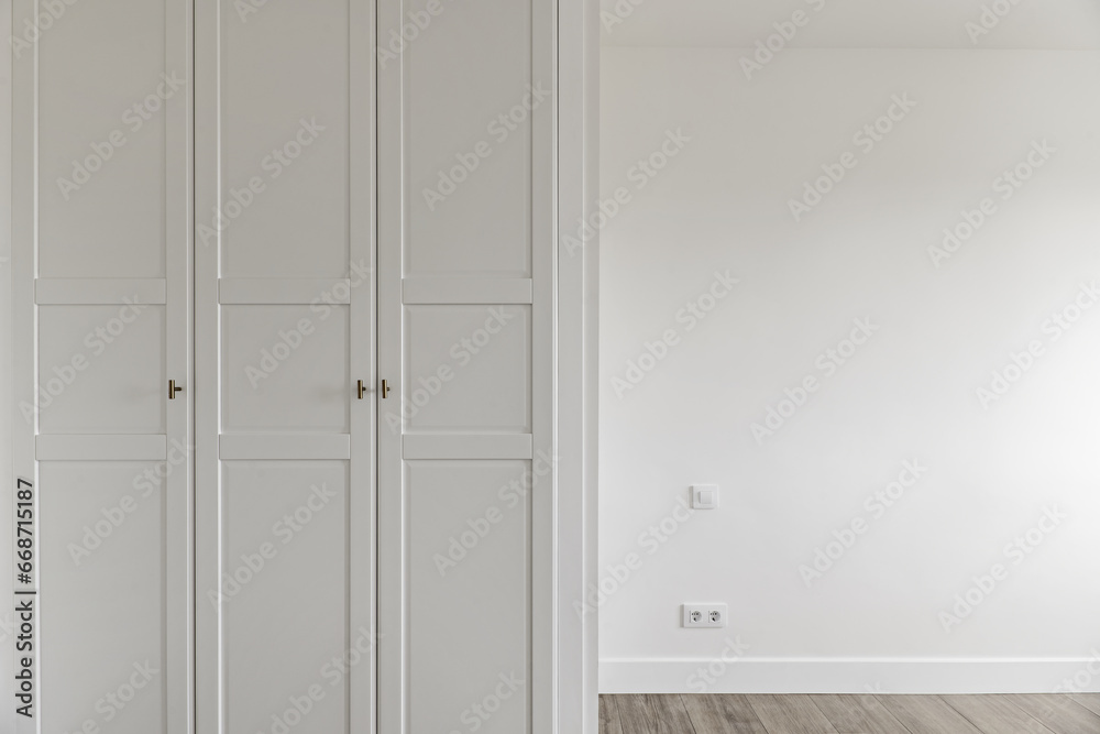 Empty room with fitted wardrobes with white wooden doors with access door and matching baseboards