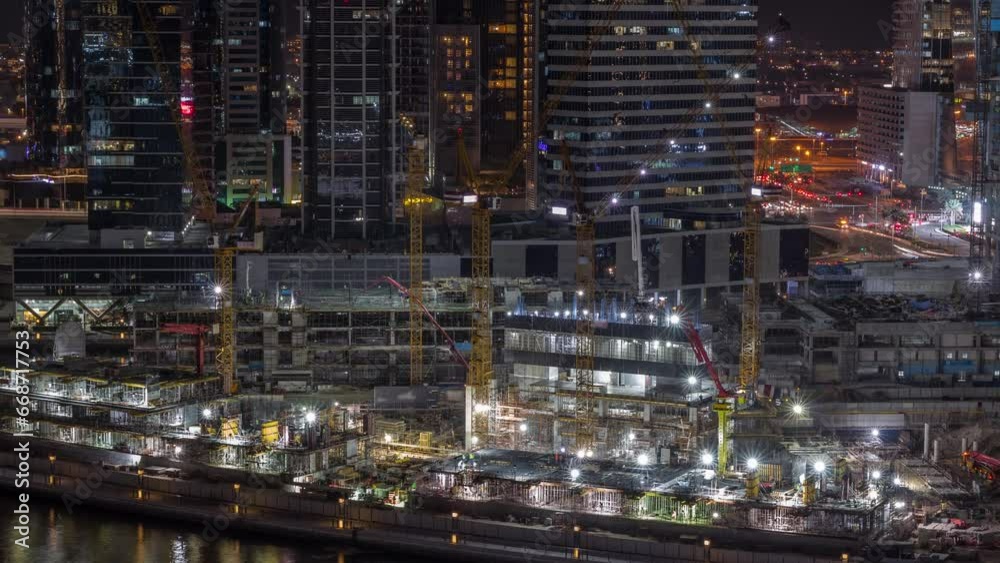 Large construction site with many working cranes night timelapse. Illuminated skyscrapers behind. Top aerial view of big development of residential and office district in Business bay, Dubai Large construction site with many working cranes night timelapse. Illuminated skyscrapers behind. Top aerial view of big development of residential and office district in Business bay, Dubai