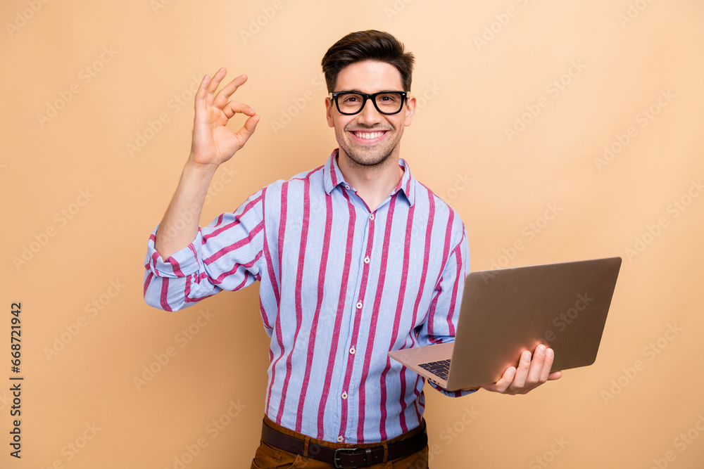 Photo of young cheerful business guy manager show okey gesture got deal in ecommerce using laptop isolated on beige color background Photo of young cheerful business guy manager show okey gesture got deal in ecommerce using laptop isolated on beige color background
