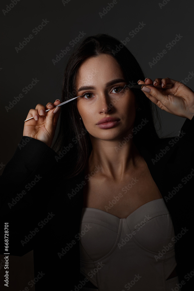 Obraz premium beautiful woman holding eyelashes tweezers on black background