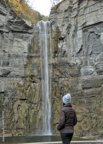 woman looking at a waterfall in Taughannock Falls State Park  cayuga lake near ithaca  upstate new york  in autumn with fall foliage  leaves changing colors  wearing brown jacket  hat
