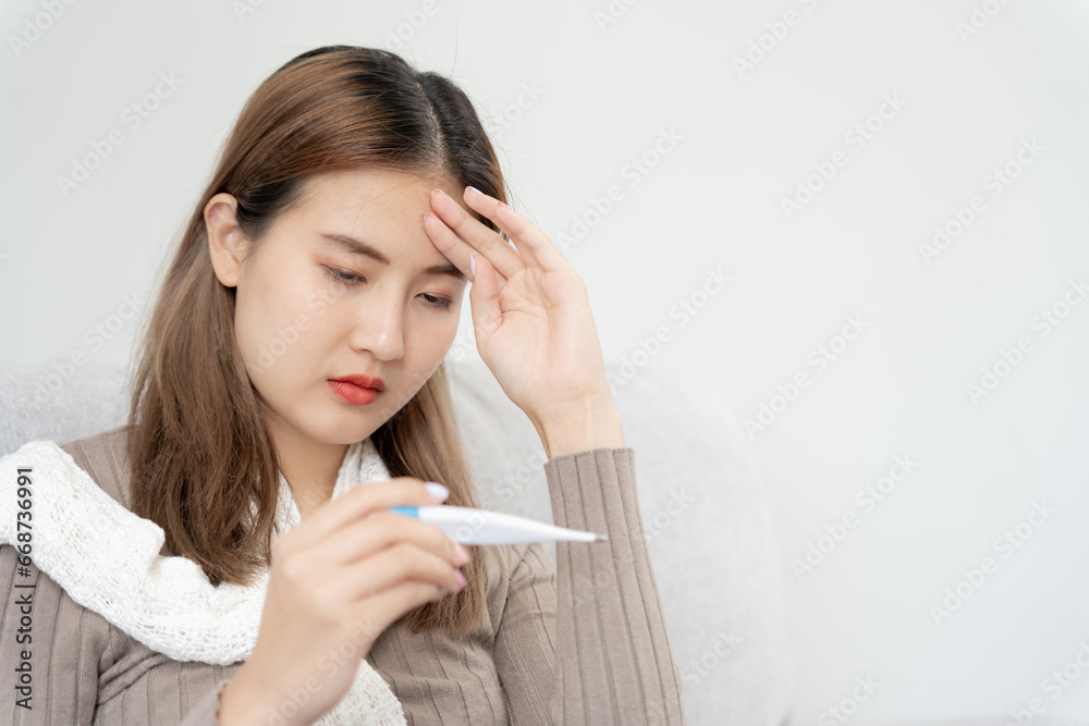 Young Asian woman having high fever while checking body temperature, female sneezing and runny nose with seasonal influenza, allergic, digital thermometer, virus, coronavirus, illness, respirator Young Asian woman having high fever while checking body temperature, female sneezing and runny nose with seasonal influenza, allergic, digital thermometer, virus, coronavirus, illness, respirator