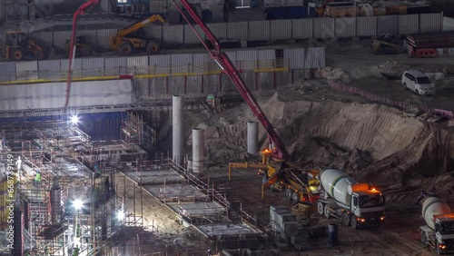 Piles in foundation pit for construction of apartment complex building aerial night timelapse. Deep installation and excavation with heavy machinery as concreete mixer and pump, bulldozers in Dubai photo