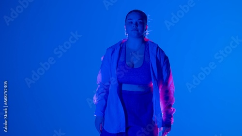 Attractive woman posing, looking at the camera in pink and blue neon light in a studio. Medium full.