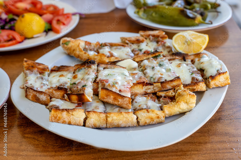 Turkish pita with minced meat and cheddar cheese on a white plate.
