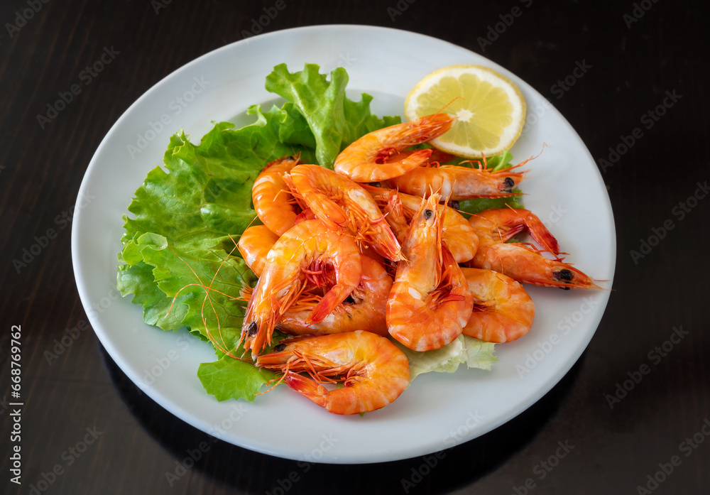 Mediterranean seafood dish of boiled shrimp on a plate in greens with lemon. On a black background. Mediterranean seafood dish of boiled shrimp on a plate in greens with lemon. On a black background.