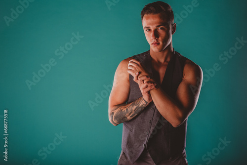 Confident fit man showcasing muscular transformation, flexing biceps and showing defined chest and abs. Motivated fitness instructor and model. Sporty strength and inspiration on turquoise background.