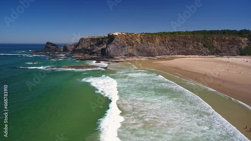 Aerial video filming by drone of the sea bay and beach near the village of Odeceixe Alentejo Portugal. Tourists surfers in the water with rocks in the background.