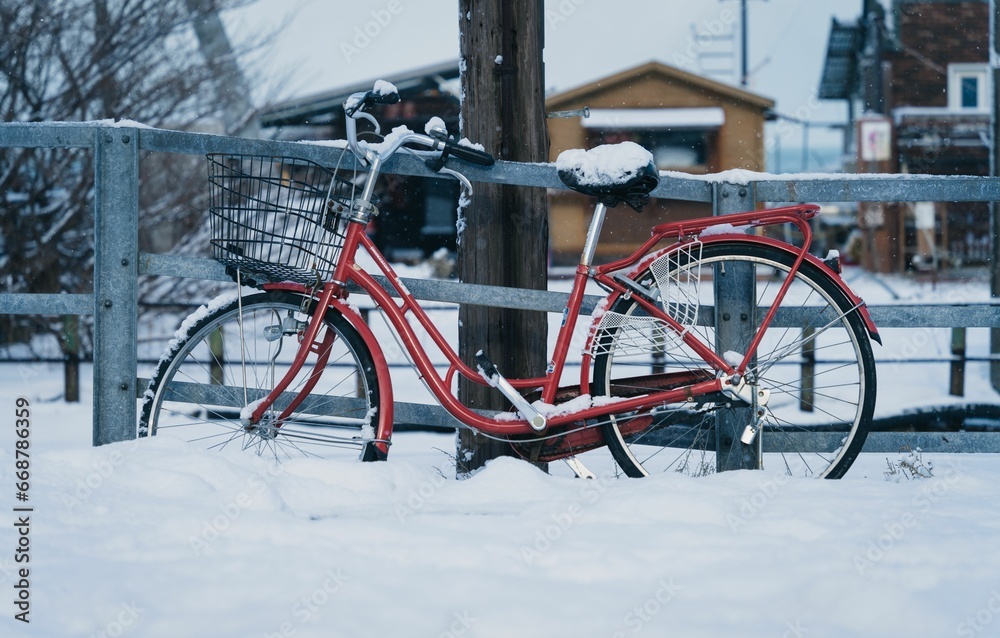 a red bicycle standing in the snow near a wooden fence