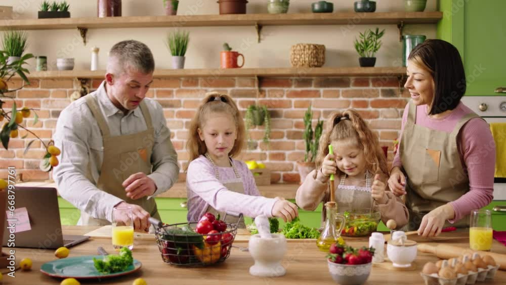 Caucasian family two small girls mom and dad at the kitchen in the morning preparing a healthy lunch they cut some vegetables and salad all together cooking together