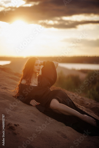Beautiful woman relaxing on the beach at sunset wearing a black dress and closed eyes. Concept for wellness, travel, relaxation or meditation.