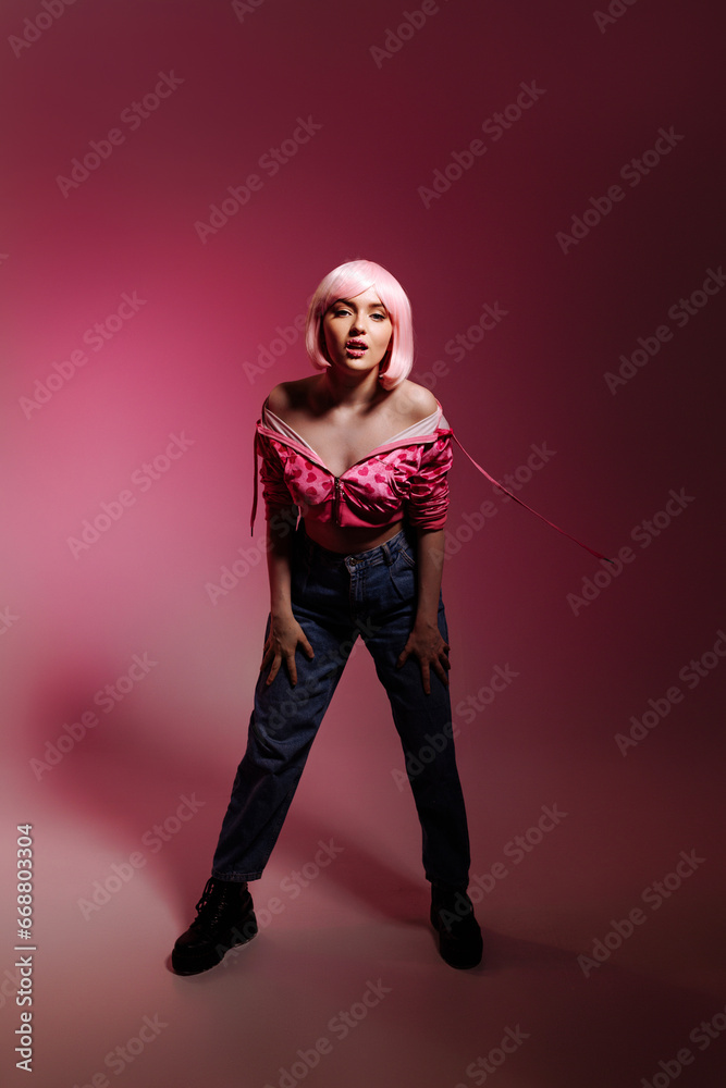 Obraz premium Stylish woman with pale pink hair wearing a pink jacket and jeans poses confidently against a pink background. Fashion advertising concept, individuality and confidence.