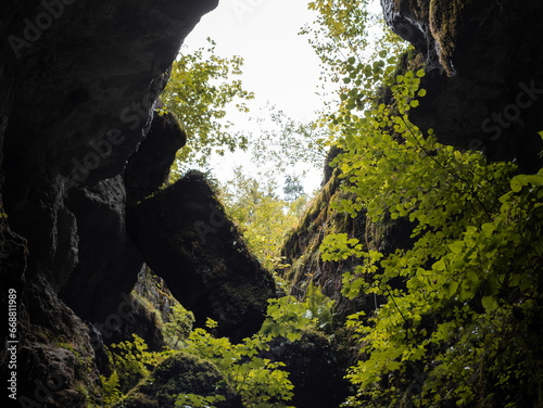 Vegetation on big rocks in the mountains. Viewing out of a cave in the sky. The idyllic nature is overgrowing the dark stones. Outdoor adventure in a German Forest.