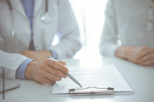 Doctor and patient discussing current health questions while sitting near of each other and using clipboard at the table in clinic  just hands closeup. Medicine concept