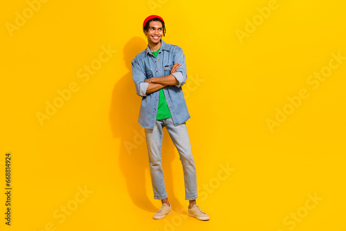 Full length photo of cute young male folded arm look empty space dressed stylish jeans garment isolated on yellow color background