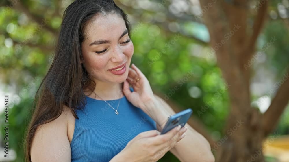 Young beautiful hispanic woman using smartphone celebrating at park Young beautiful hispanic woman using smartphone celebrating at park