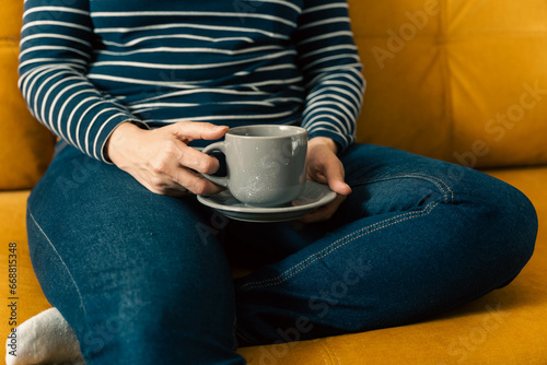 woman in a striped sweater sits on the sofa and holds a cup of coffee in hands