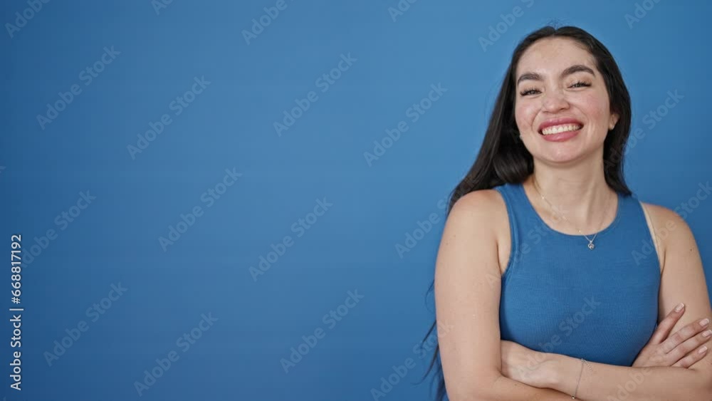 Young beautiful hispanic woman standing with arms crossed gesture saying yes with hand over isolated blue background Young beautiful hispanic woman standing with arms crossed gesture saying yes with hand over isolated blue background