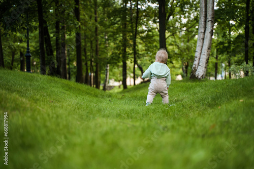 Cute blonde baby toddler in the park, there is a lot of green grass around. The concept of a happy childhood, a place for text